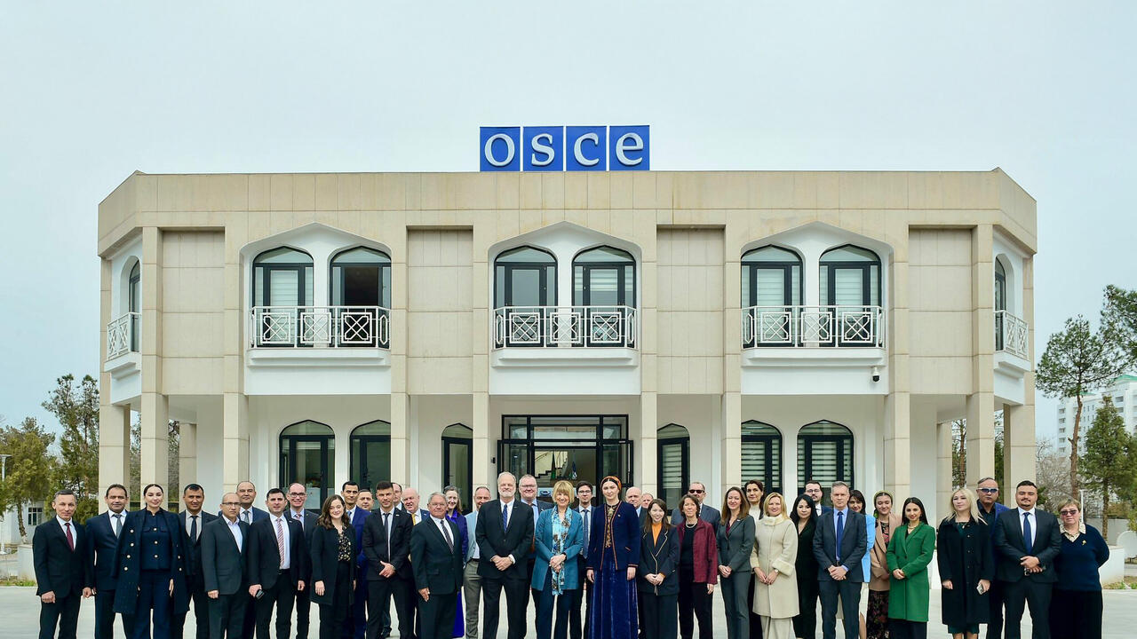 A group of people stands in front of a building labeled OSCE.